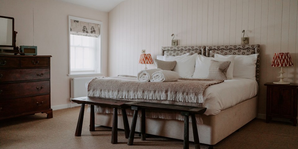 Hotel room with bed, wooden stools, and antique dresser.