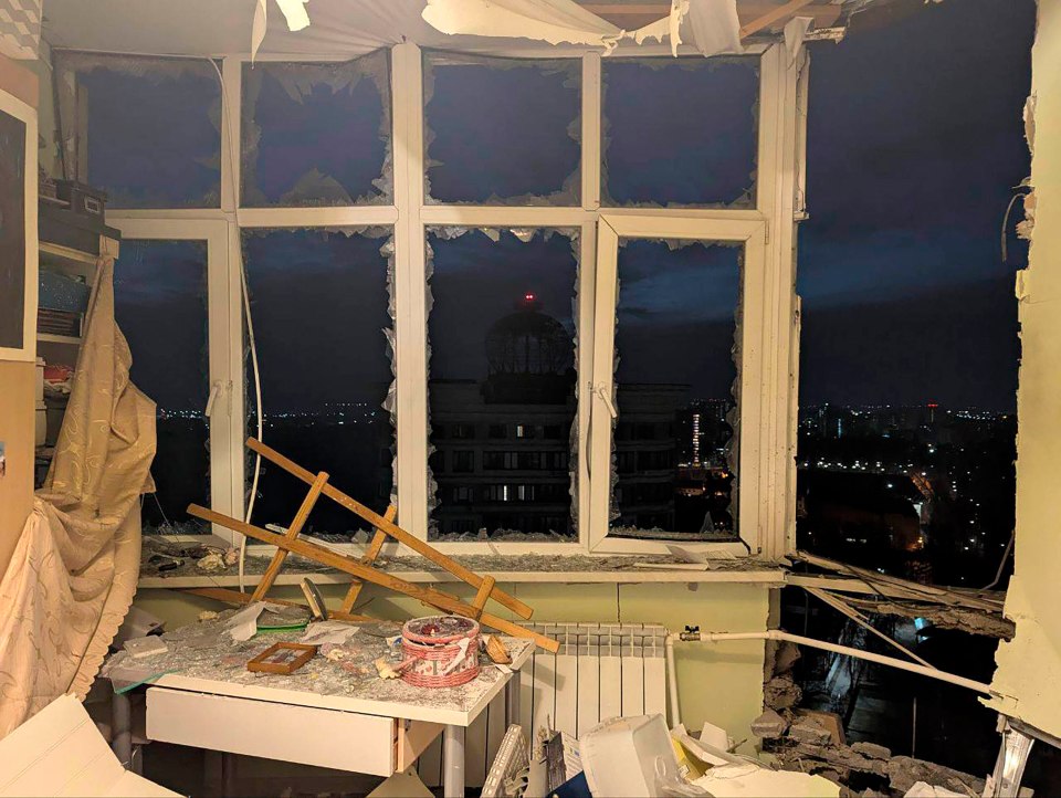 Damage to a room from a drone attack, showing a shattered window and debris.