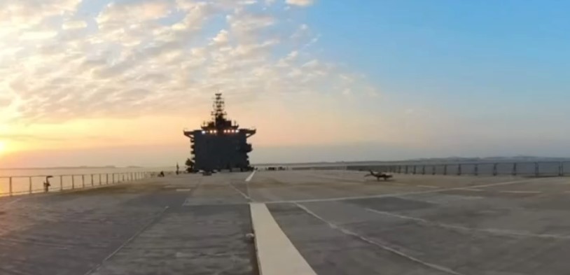 A small toy fighter jet on the deck of a ship at sunset.