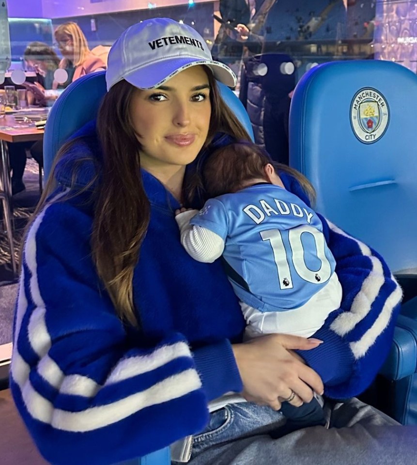 Woman holding baby in Manchester City jersey.