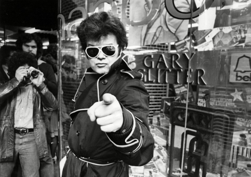 Black and white photo of Gary Glitter signing autographs for fans.