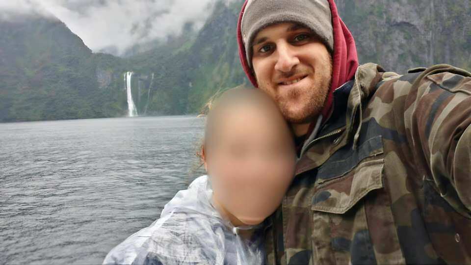 Selfie of a man with a blurred face of a child in front of a waterfall.