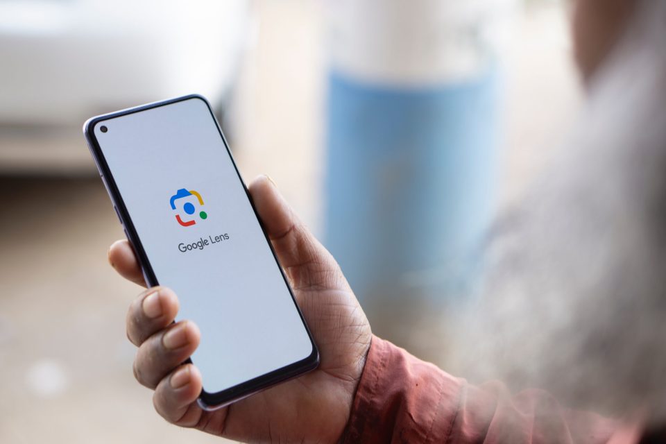 Person holding a smartphone displaying the Google Lens app.
