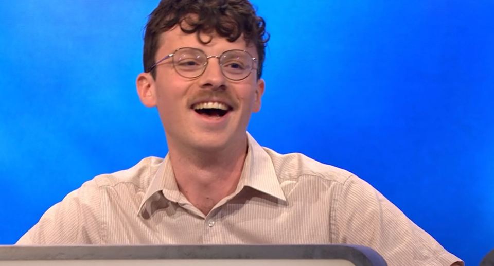 A man with glasses and a mustache laughs.