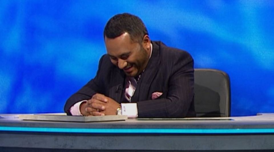 Man in suit laughing at a game show desk.