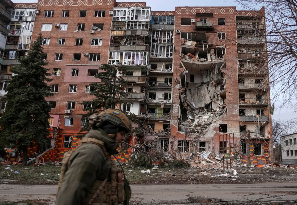 Ukrainian serviceman walking past a bomb-damaged residential building.