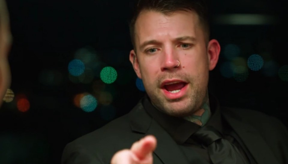 A man in a suit angrily speaks to someone off-camera.