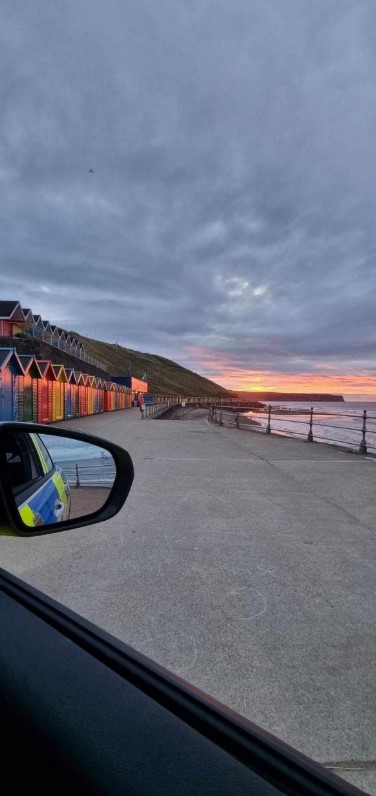 Sunset over Whitby coast with colorful beach huts.