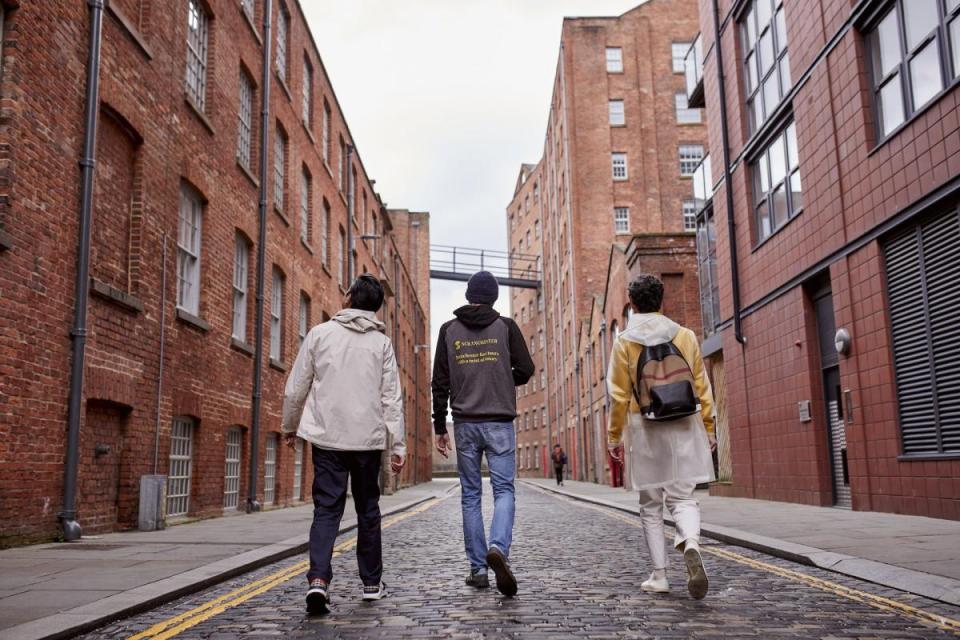 Three people walking down a brick street in Ancoats.