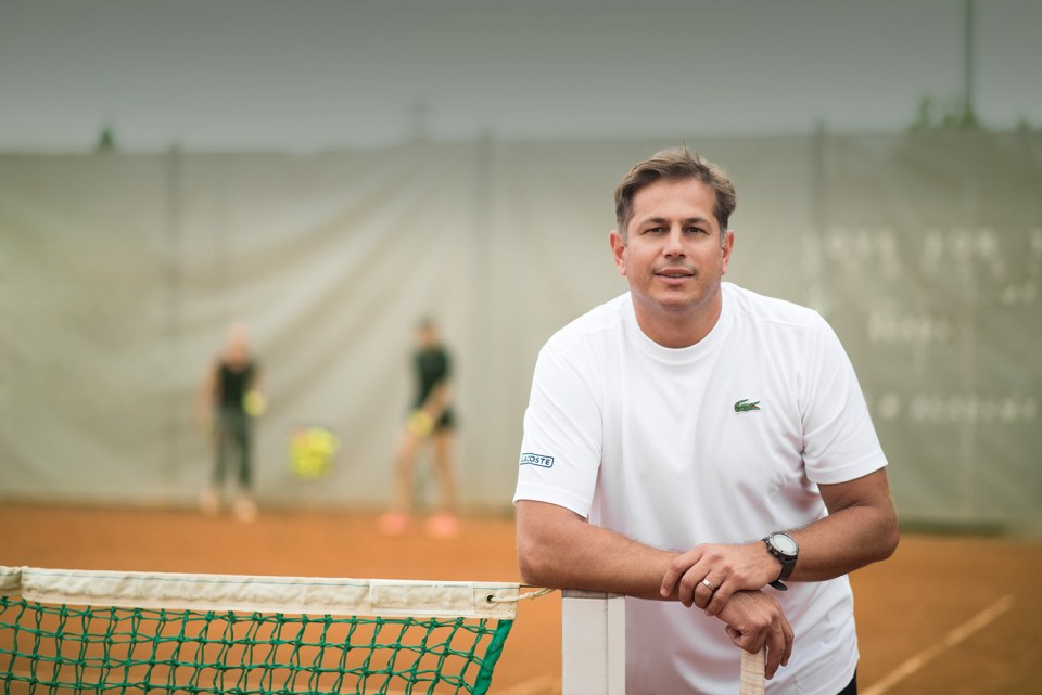 Man in white tennis shirt leaning on tennis net.