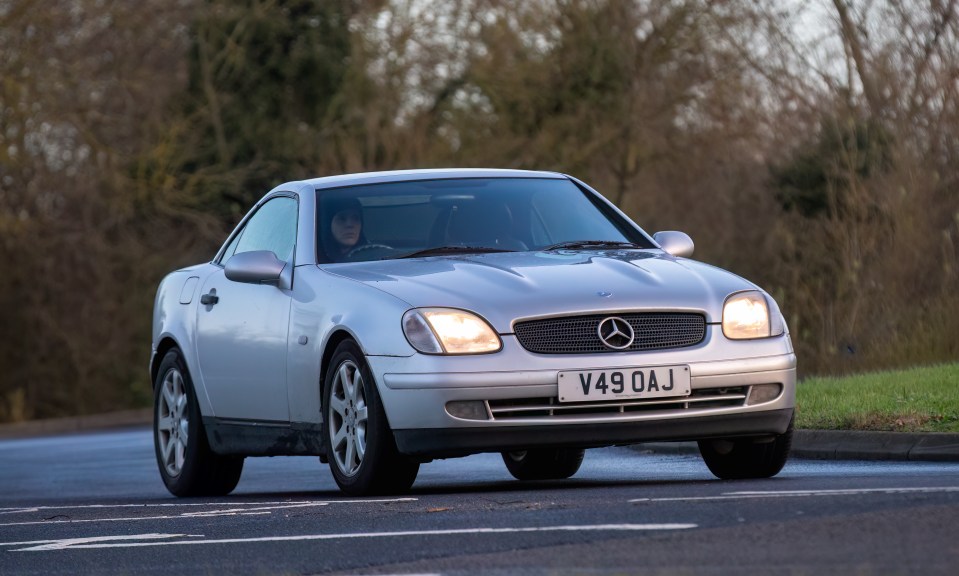 Silver 1999 Mercedes-Benz SLK driving on a road.