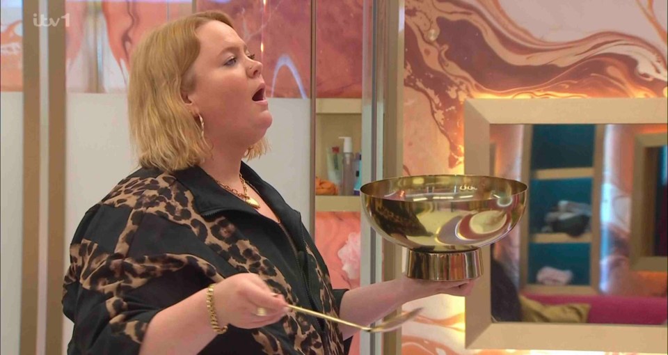 A woman in a leopard-print shirt holds a large golden bowl and a long spoon in a bathroom.