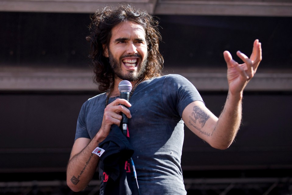 Russell Brand speaking into a microphone at a rally.