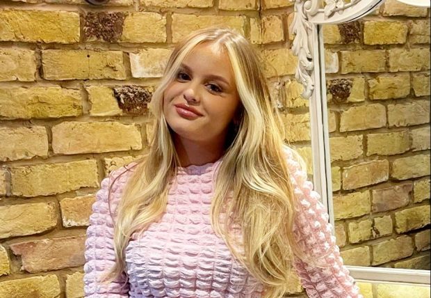 Woman in pink textured top and light wash jeans leaning on a bathroom sink.