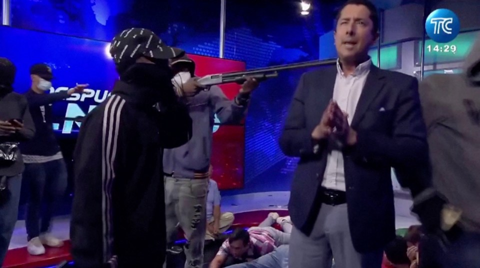 Screengrab of a man pointing a shotgun at a television presenter during a live broadcast.