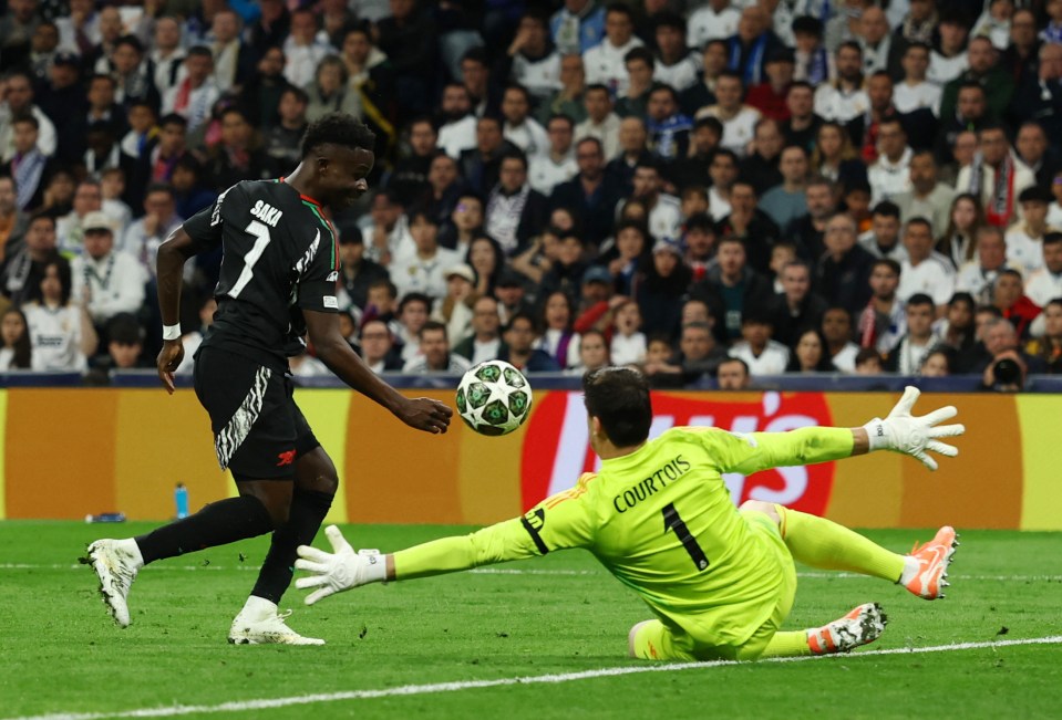 Bukayo Saka scoring a goal against Real Madrid's goalkeeper.