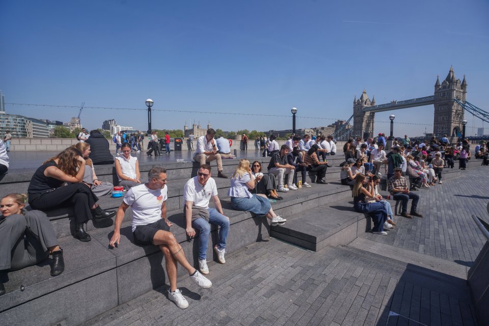 City workers relaxing on steps by the Thames, Tower Bridge in the background.