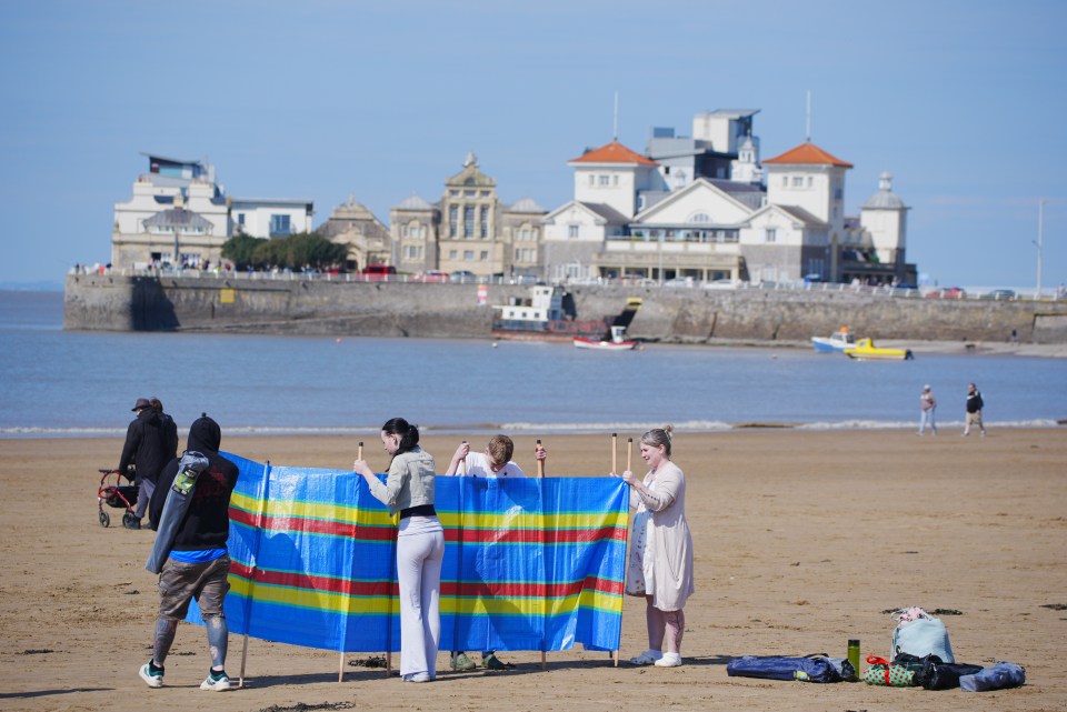 People erecting a windbreak on a beach.