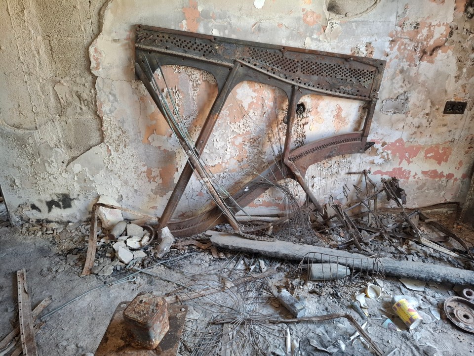 The rusted remains of a piano in a dilapidated room.