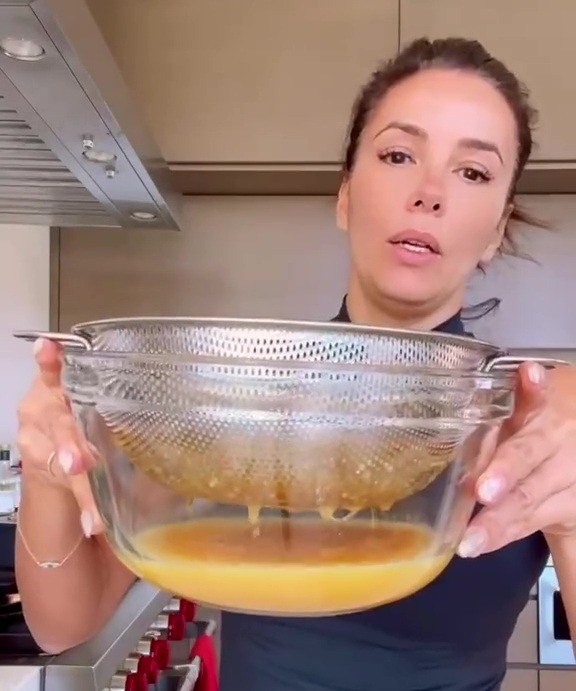 Eva Longoria holding a bowl with a strainer of yellow liquid.