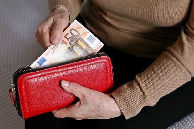 Elderly woman taking a fifty euro note from her red wallet.