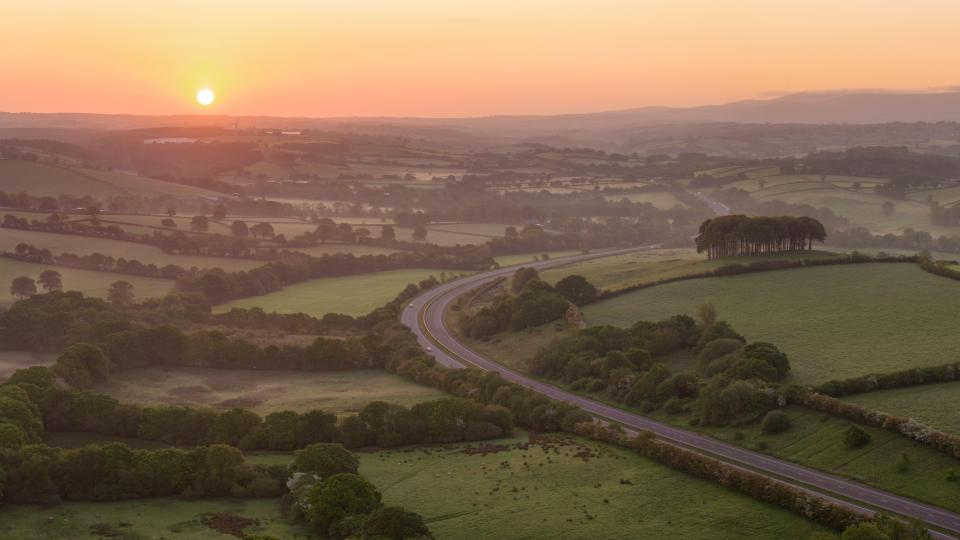 Sunrise over a winding road in a rural landscape.