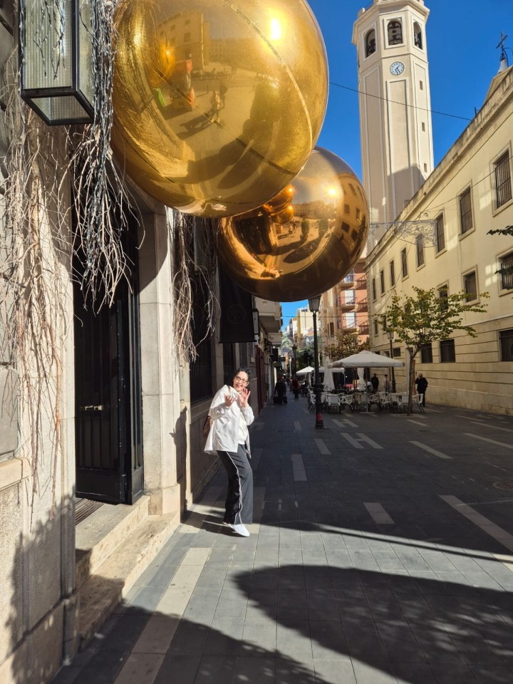 Woman standing near large gold orbs in Alicante, Spain.