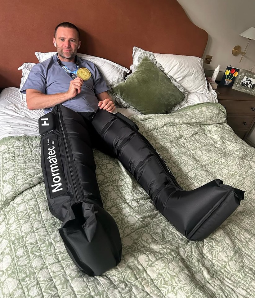 Man in bed wearing a marathon medal and recovery boots.