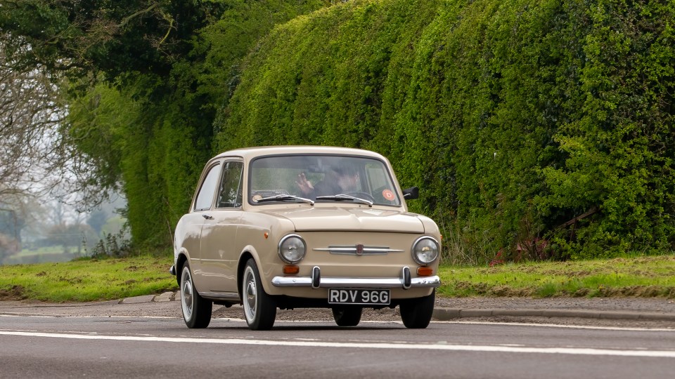 A beige 1969 Fiat 850 driving on a country road.