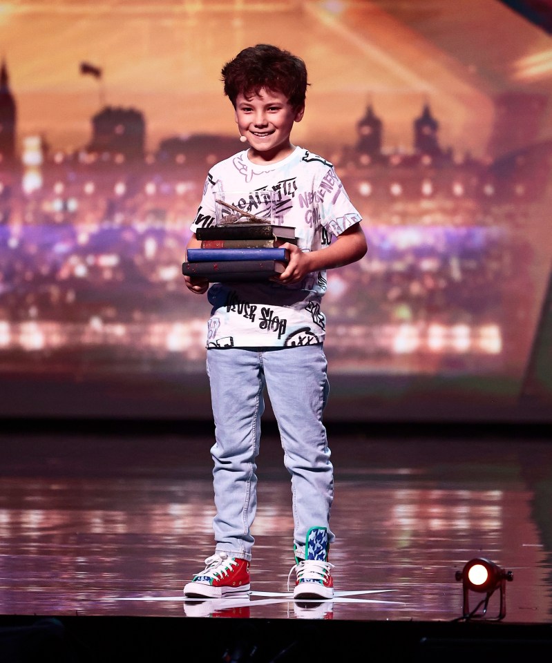 A young boy on a stage holding a stack of books.