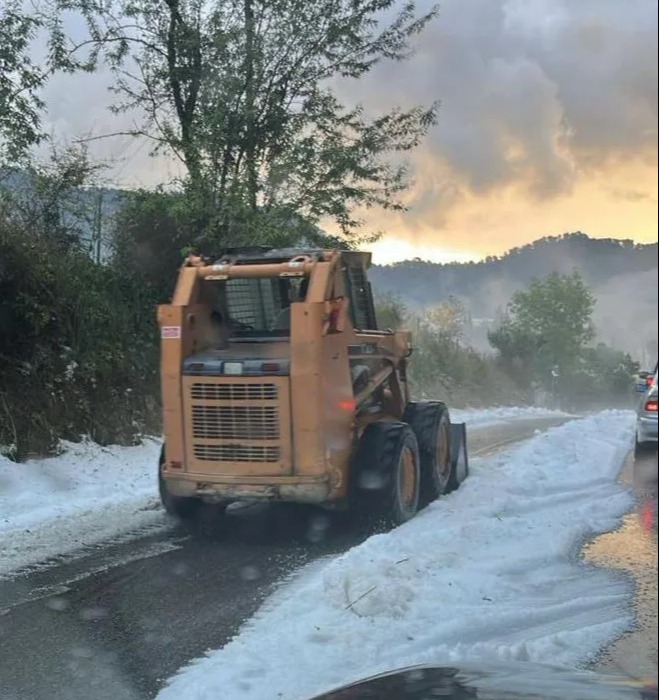A road covered in hail with a small bulldozer clearing it.