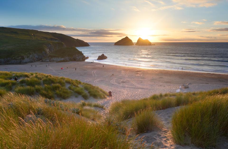 Sunset over Holywell Bay beach in Cornwall, England, with people enjoying the sand and dunes.