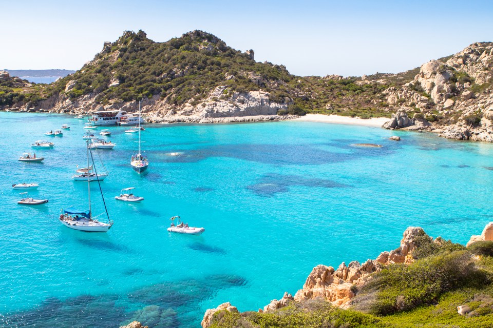 Cala Corsara beach in Sardinia, Italy, with boats in turquoise water.