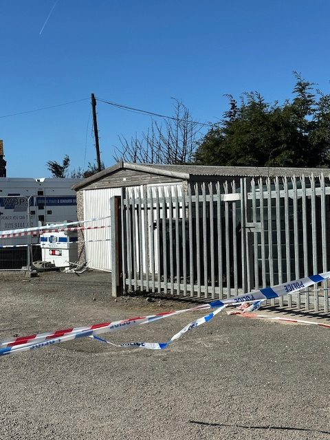 Crime scene with police tape and a building behind a fence.