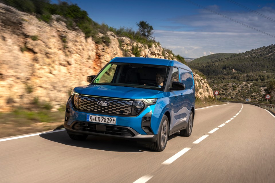 Blue Ford Transit van driving on a winding road.