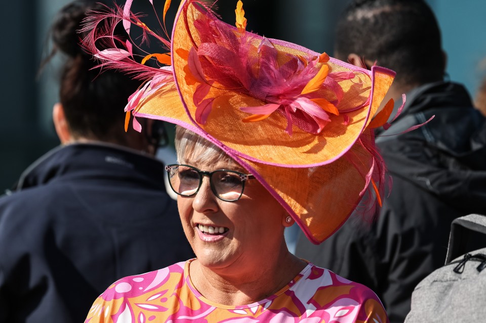 Woman wearing a large orange and pink hat with feathers.