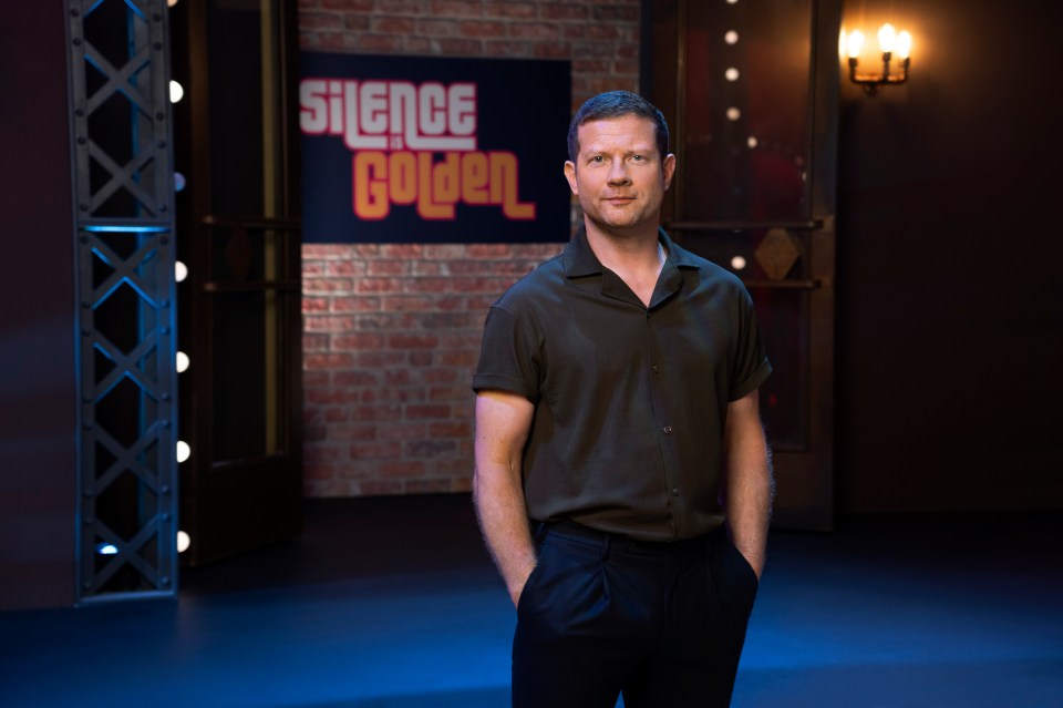 A man standing on a stage in front of a "Silence is Golden" sign.