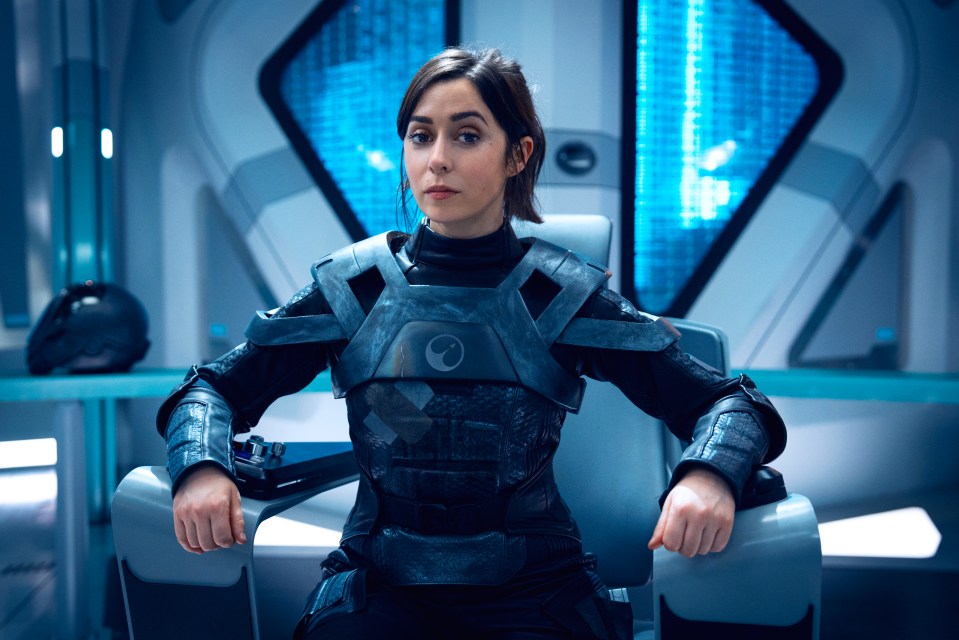Woman in futuristic armor seated in a chair.