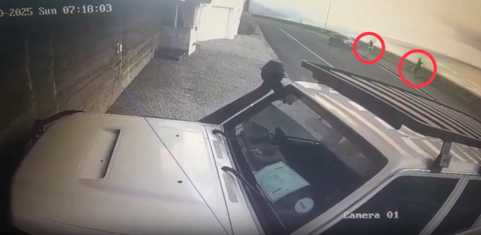 Security camera footage of a vehicle parked near a road, with two people visible in the distance.