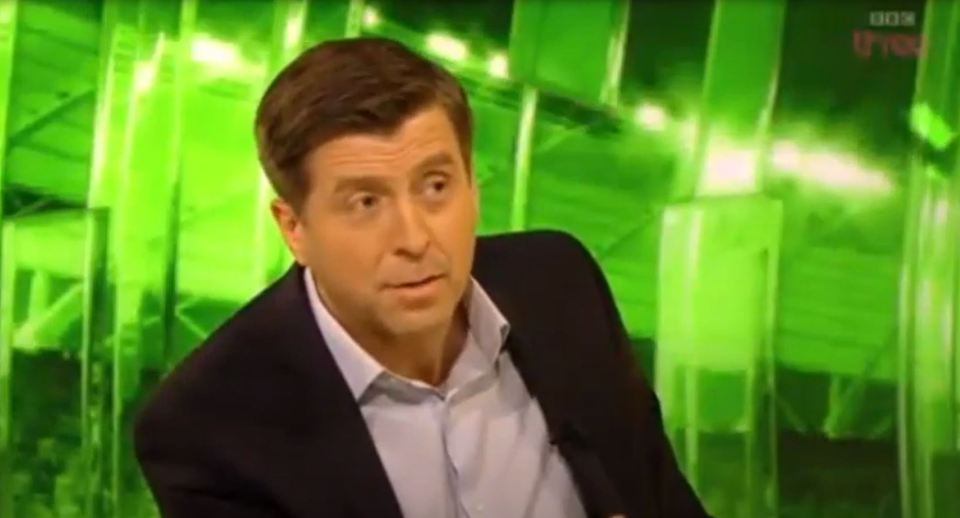 Man in suit speaking in front of a green background.