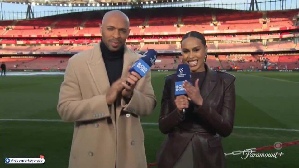 Two sports reporters holding microphones in front of a soccer stadium.