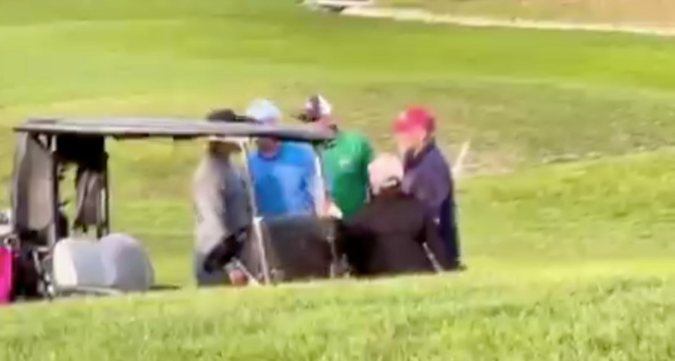 Golfers gathered around a golf cart on a golf course.
