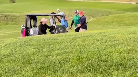Golfers by a golf cart on a course.