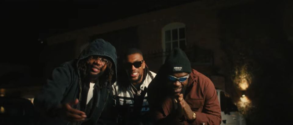 Three men posing outdoors at night.