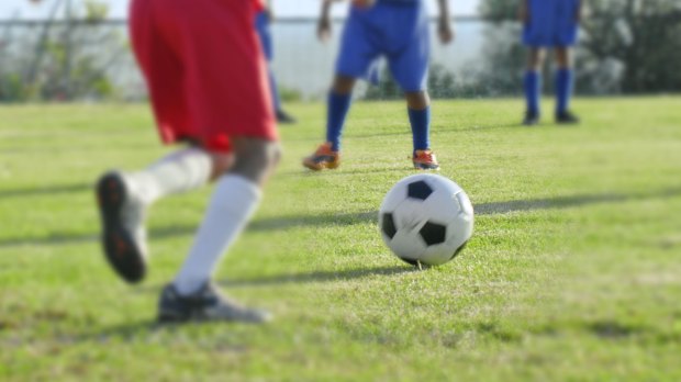 Soccer ball on a field with children playing in the background.
