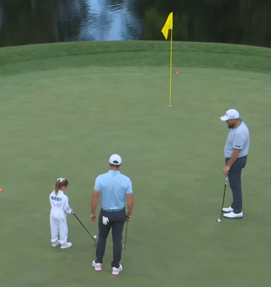 A young girl putts on a golf green, watched by two men.