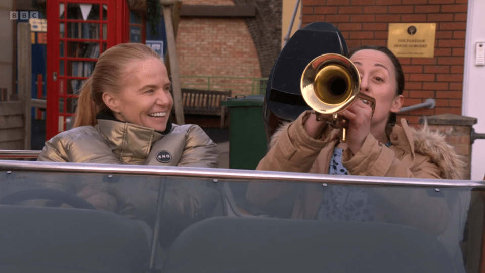 Two women in a car; one plays a trumpet.