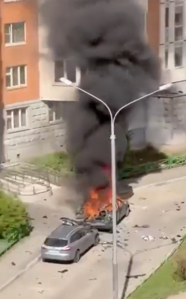 Screenshot of a burning car emitting thick black smoke near a residential building.