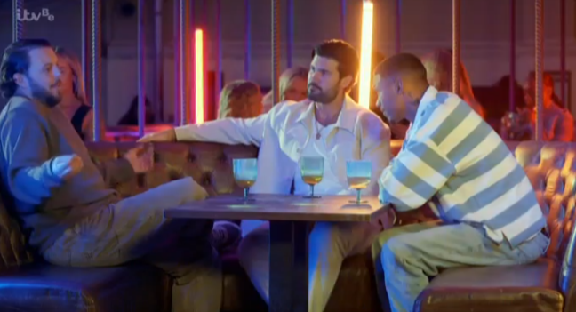 Three men sitting at a table in a bar, talking.