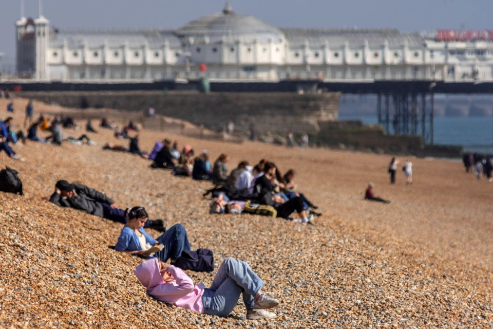 People relaxing on a pebble beach in front of a pier.